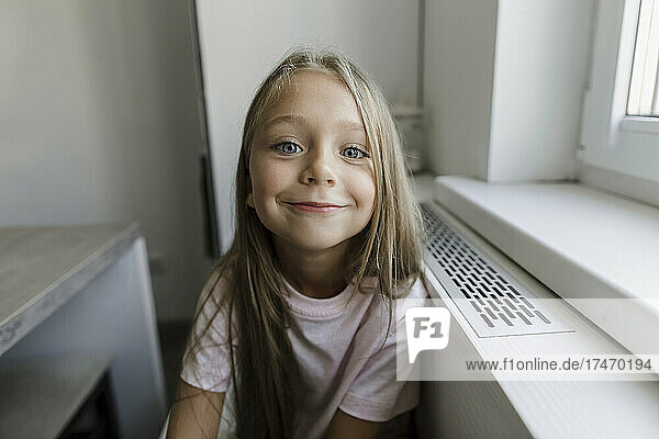 Smiling blond girl sitting at window