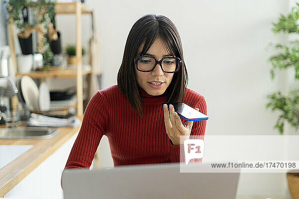 Businesswoman using laptop talking on smart phone at home office