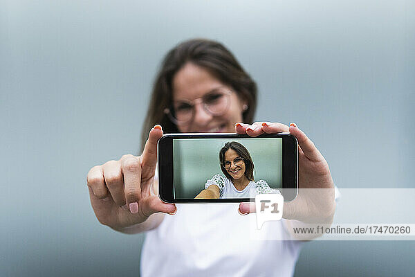 Smiling young woman photographing through smart phone