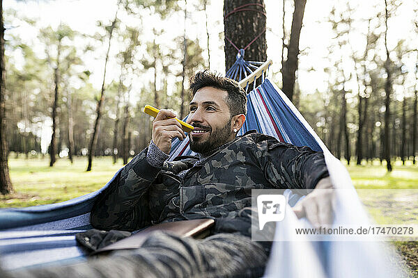 Smiling man lying in hammock making voicemail through smart phone at park