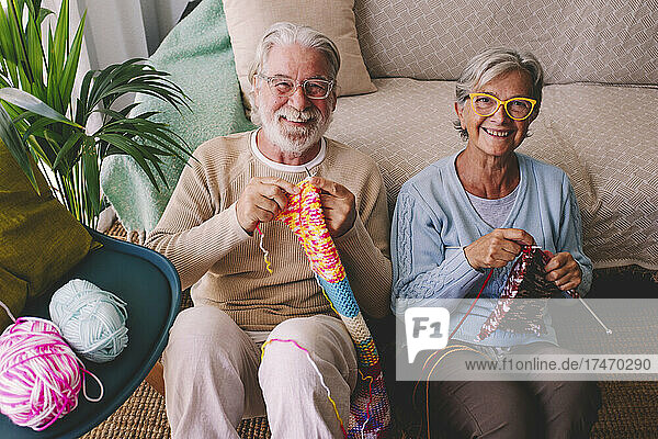 Smiling senior couple knitting wool at home