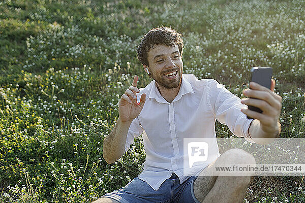 Happy man taking selfie through mobile phone on meadow