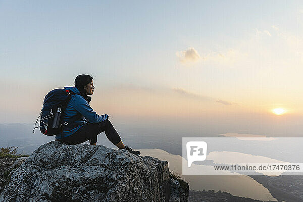 Wanderer mit Rucksack blickt auf den Sonnenuntergang auf einem Felsen