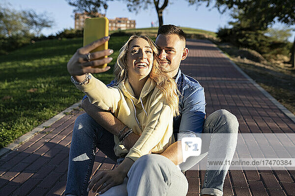 Smiling girlfriend taking selfie with boyfriend through mobile phone at sunset