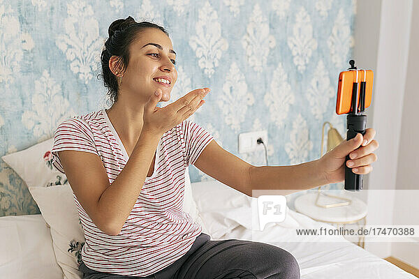 Smiling female influencer vlogging through mobile phone in bedroom