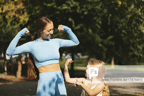 Mother and daughter showing biceps to each other on sunny day