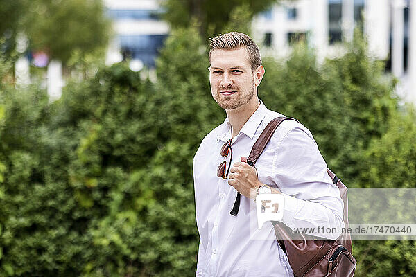 Young businessman holding backpack at park