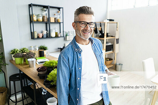 Smiling man wearing eyeglasses holding coffee cup at home
