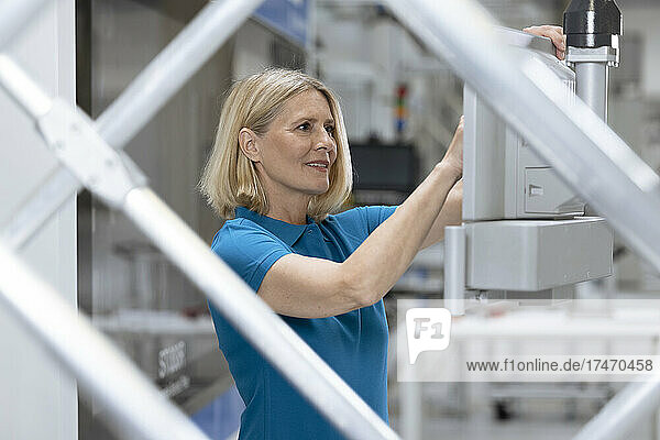 Female professional operating machinery seen through railing in industry