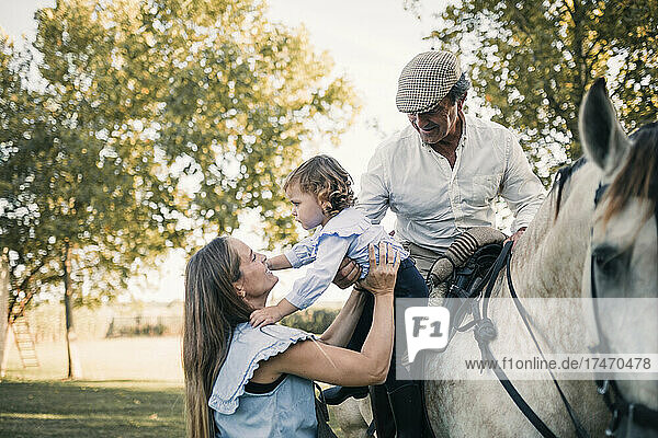 Mutter trägt Tochter  während älterer Mann auf Pferd sitzt