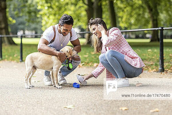 Lächelnde Frau gibt Hund von Freund im Park Wasser