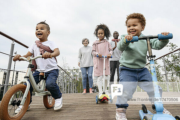 Happy children playing with push scooters and bicycle on bridge