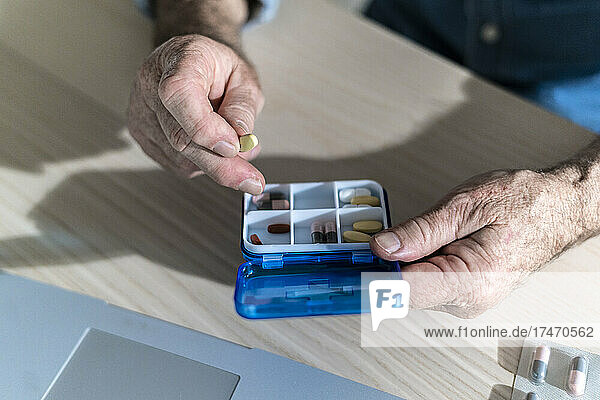 Hands of senior man taking out medicine from pill box at dining table