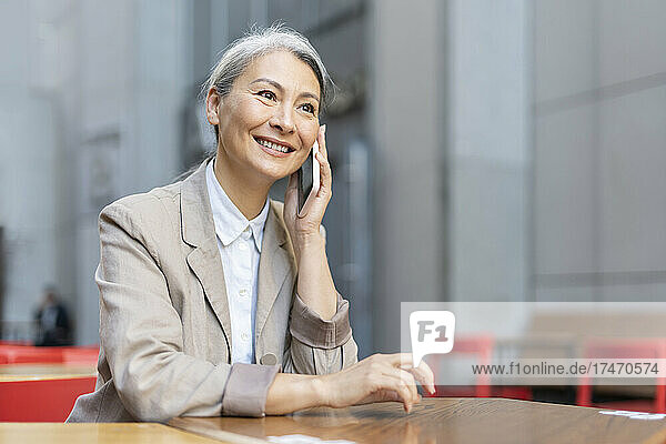 Mature woman smiling while talking on mobile phone at sidewalk cafe