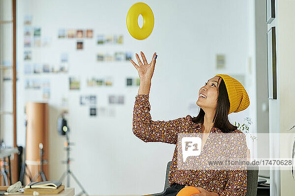 Young businesswoman wearing knit hat playing with yellow plastic ring in office