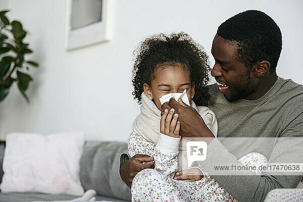 Father wiping daughter's nose at home