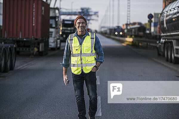 Smiling male truck driver with hand in pocket walking on street at dock