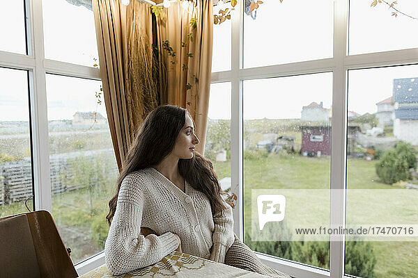 Thoughtful young woman looking through home window