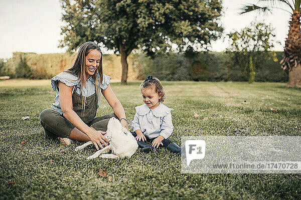 Smiling mother and daughter playing with dog at ranch
