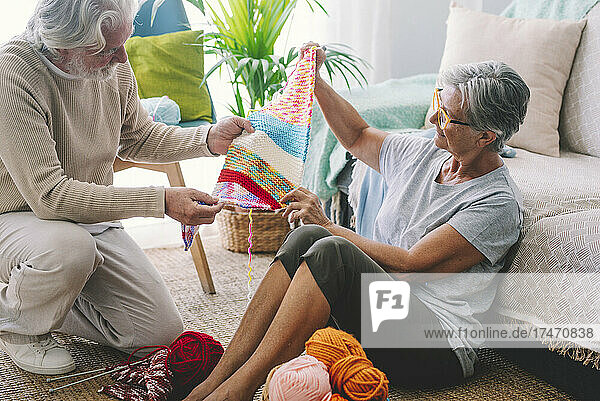 Senior woman showing knitted wool to man in living room