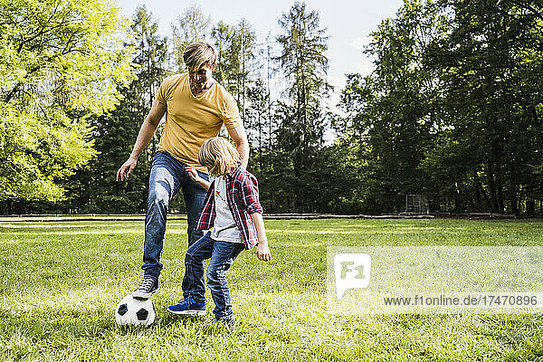 Father and son playing with soccer ball at park