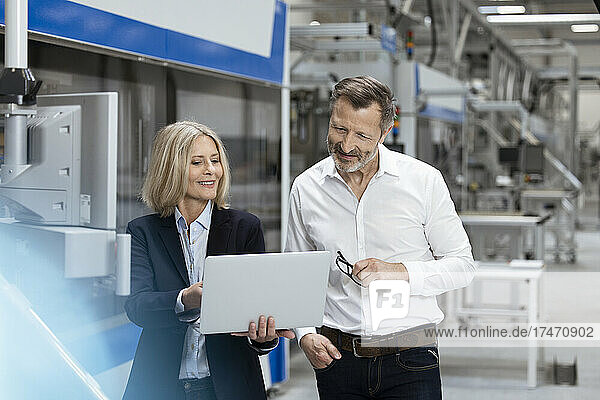 Smiling businesswoman explaining business strategy over laptop to male colleague in factory