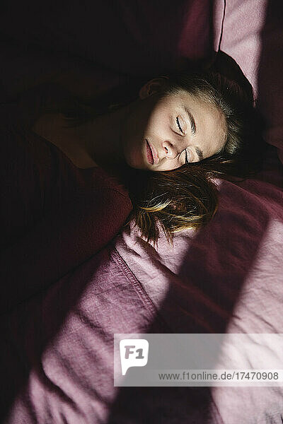Depressed young woman with eyes closed lying on bed