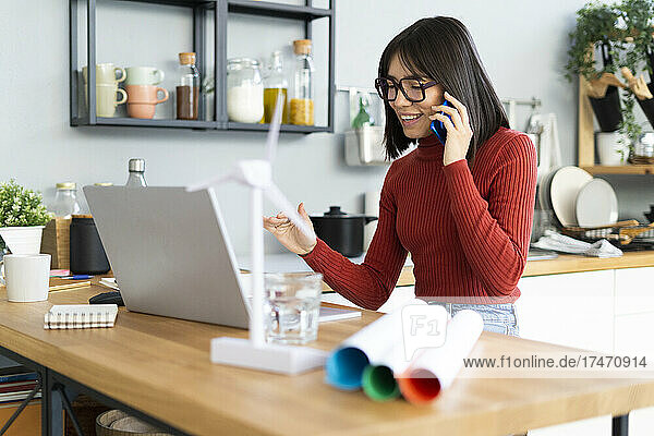 Smiling freelancer with laptop talking on mobile phone at home office