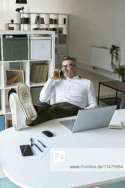 Smiling businessman with feet up talking on mobile phone in office
