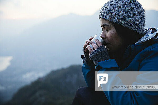 Woman wearing knit hat drinking coffee on mountain