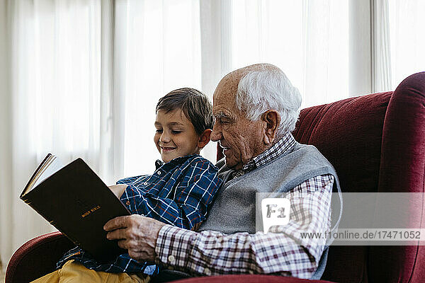 Grandfather reading bible with grandson at home
