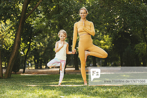 Smiling mother and daughter practicing yoga on one leg in park