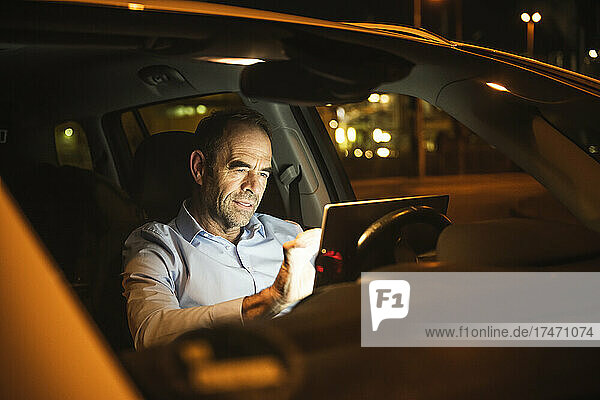 Businessman using laptop in car at night