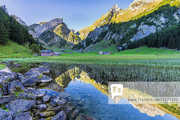 Mountains reflecting in clear water of Seealpsee lake at dawn with secluded huts in background