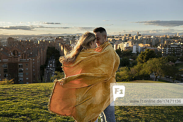 Couple wrapped in blanket standing on hill