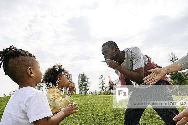 Father blowing bubble while playing with children in park