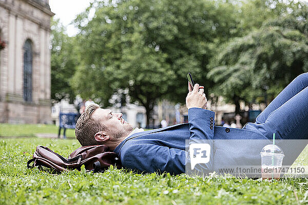 Young businessman using mobile phone while lying on grass