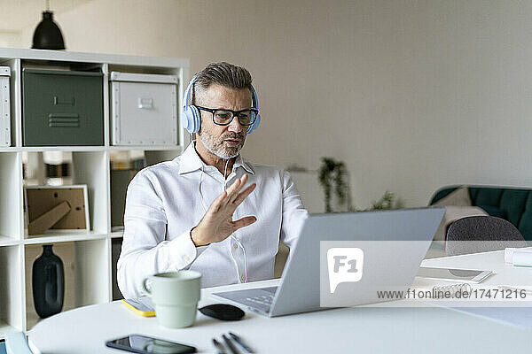 Businessman waving on video call through laptop in office