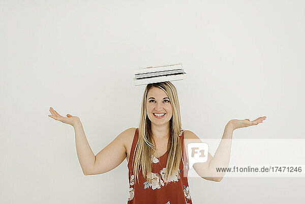 Happy woman balancing books on head in front of wall
