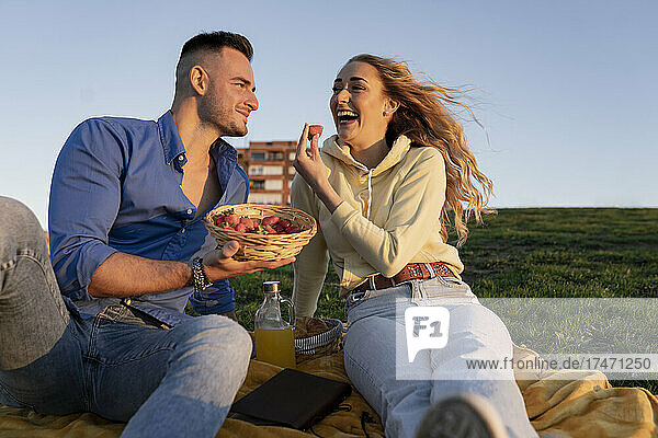 Cheerful girlfriend enjoying picnic with boyfriend on hill