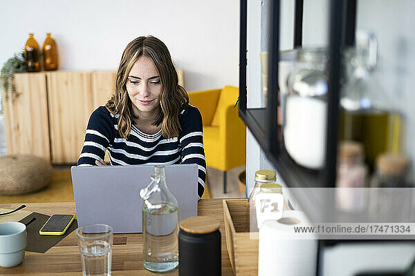 Smiling woman using laptop at kitchen counter