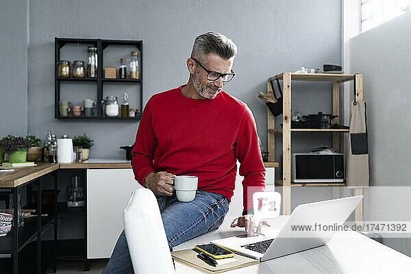 Man with coffee cup using laptop while sitting on table