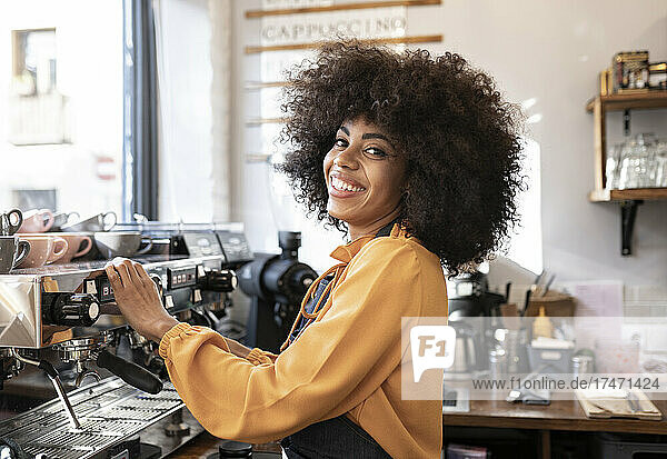 Lächelnde Kellnerin mit Afro-Frisur steht an der Kaffeemaschine