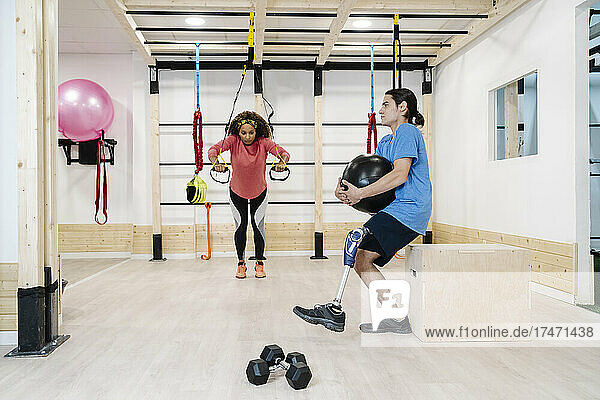 Disabled athlete holding medicine ball with friend exercising in gym
