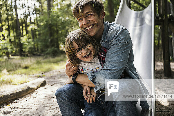 Father hugging son while sitting on slide in forest