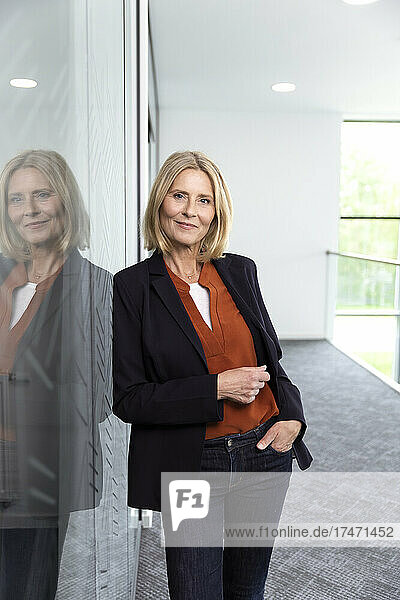 Female professional leaning on glass at corridor