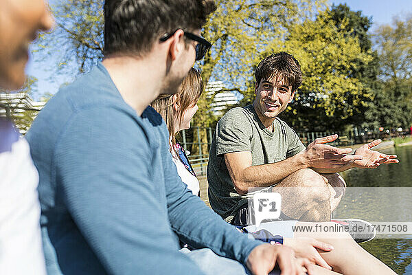 Young man talking with friends on sunny day in park
