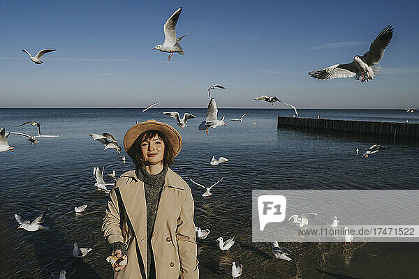 Smiling woman feeding flock of seagulls at sea