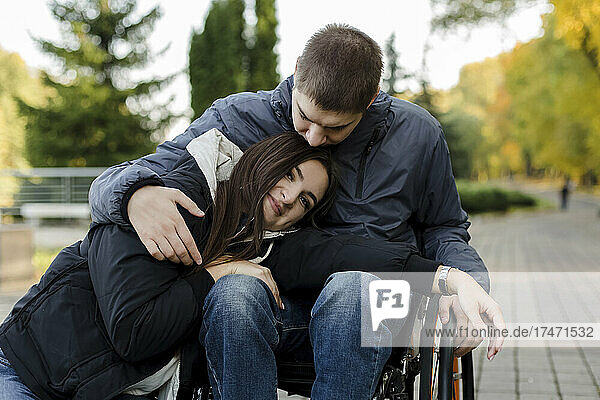 Smiling girlfriend leaning on disabled boyfriend's lap in park