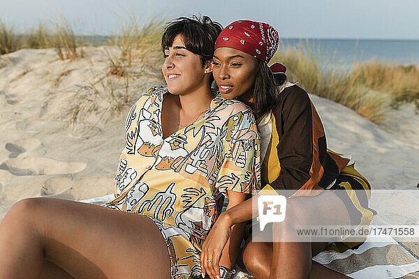 Lesbian couple sitting at beach on sunny day